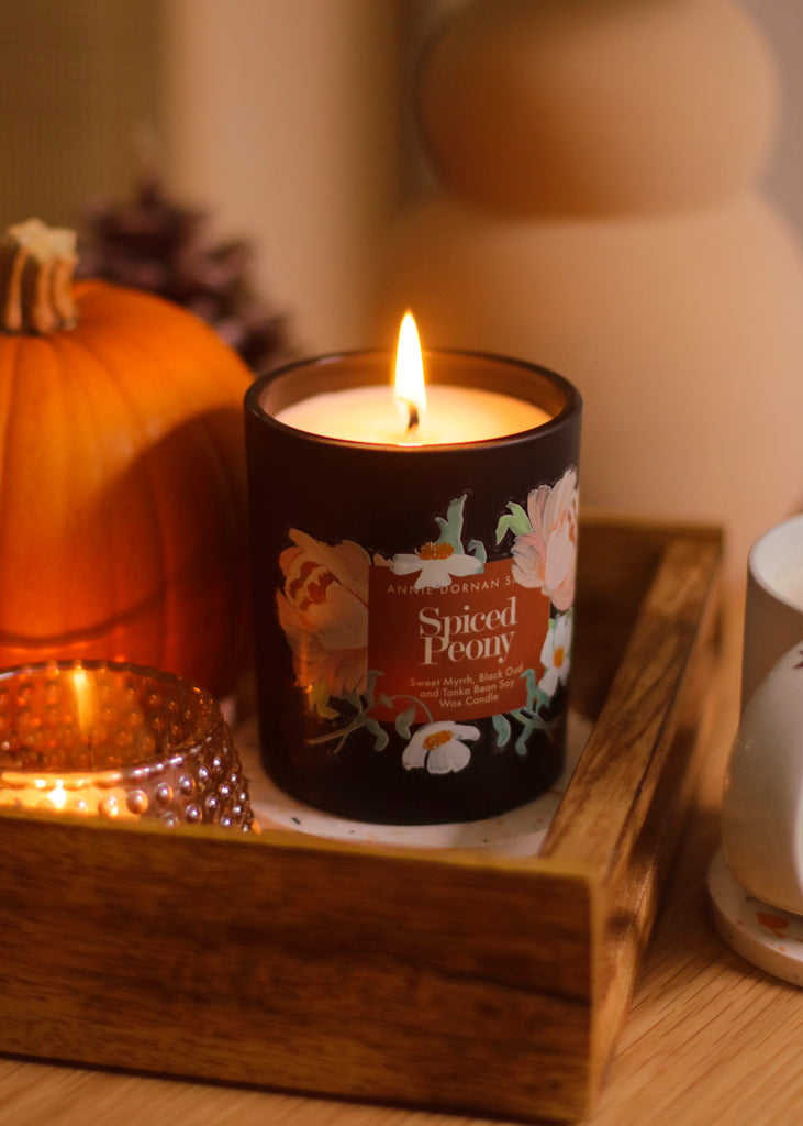 a peony scented candle, sitting in a wooden tray alongside a pumpkin