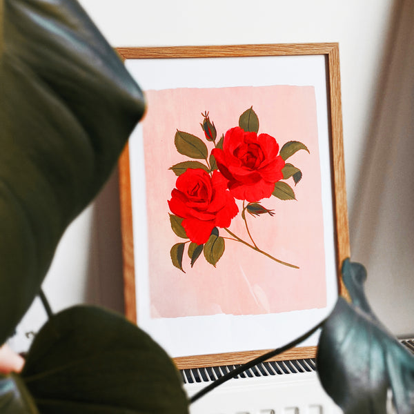 a framed print of painted roses propped on a radiator surrounded by houseplant leaves