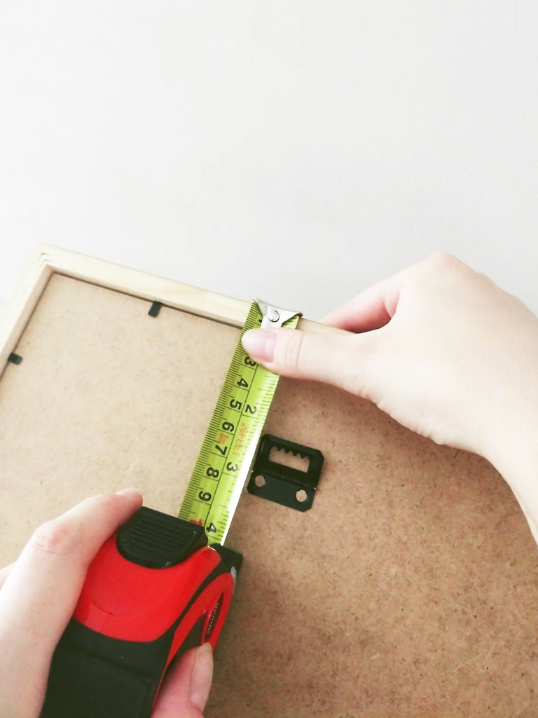 measuring the distance from the top of the frame to the hanging bracket with a tape measure 