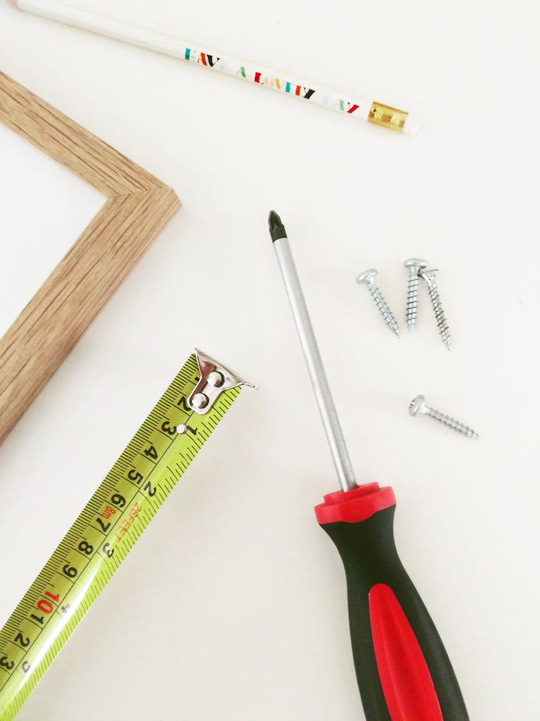 a frame, tape measure, screwdriver, pencil and screws laid out on a table