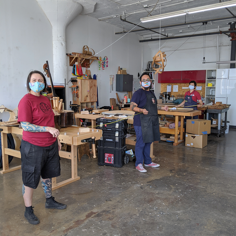 woodshop residents at their benches standing 6 feet apart holding tape measures