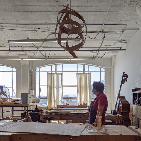 Resident Kirtan Tom looks out the window from her bench, steam bending lamp overhead