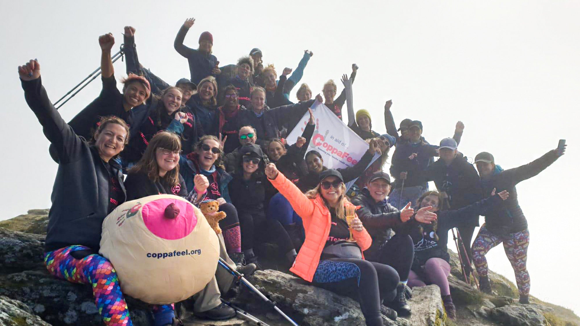 Photo showing a group of hikers holding their arms aloft while sat on a mountain top.