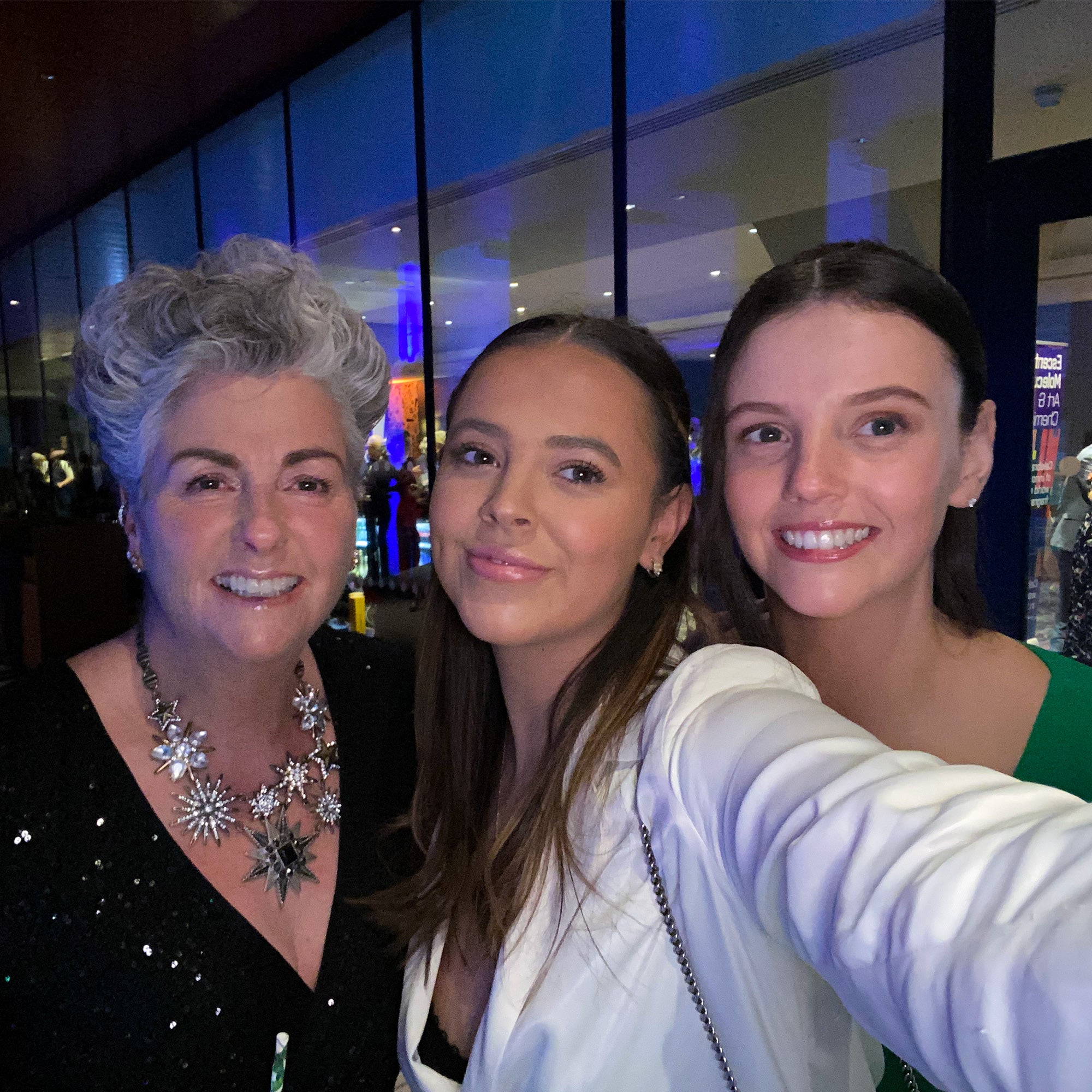 Photo showing Maxine, Margot and Darcy Laceby smiling at the camera as they take a selfie, they are sitting indoors at an awards venue and dressed in glamorous evening wear