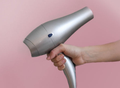 Person holding hair dryer against pink background. How to get your hair longer and stronger