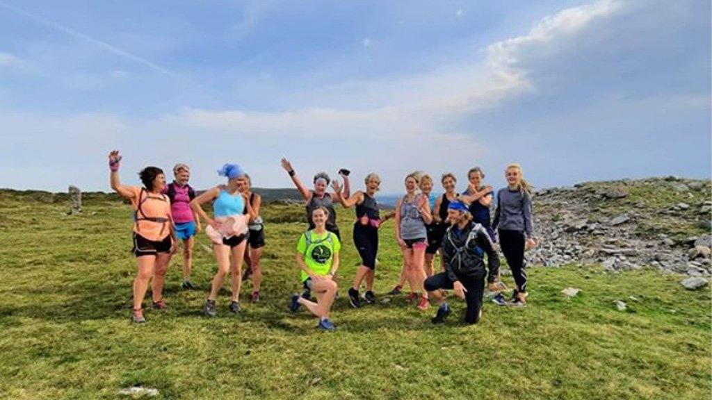 Photo showing a group of women in colourful running gear standing on a hill against a blue sky while a man crouches in front of them