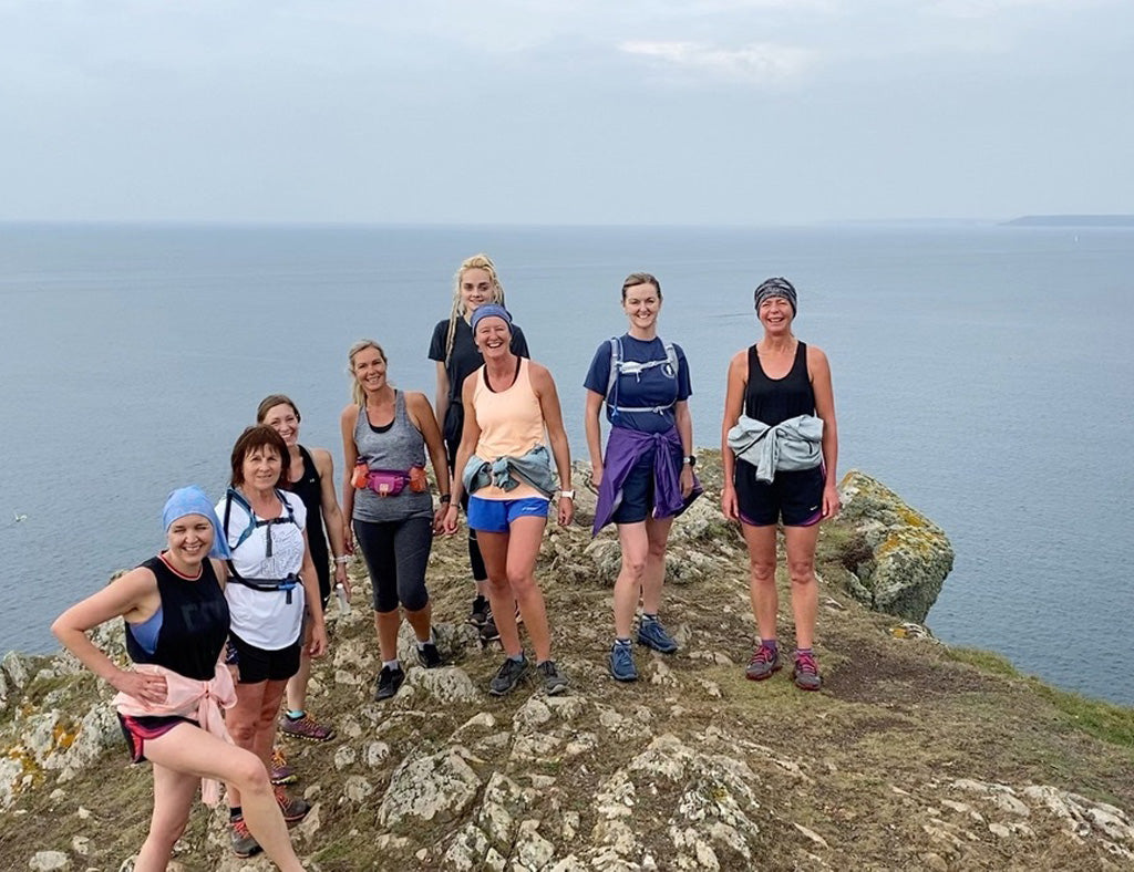 Photo showing a group of white women in running clothes standing on a grassy headland against a grey sky and sea