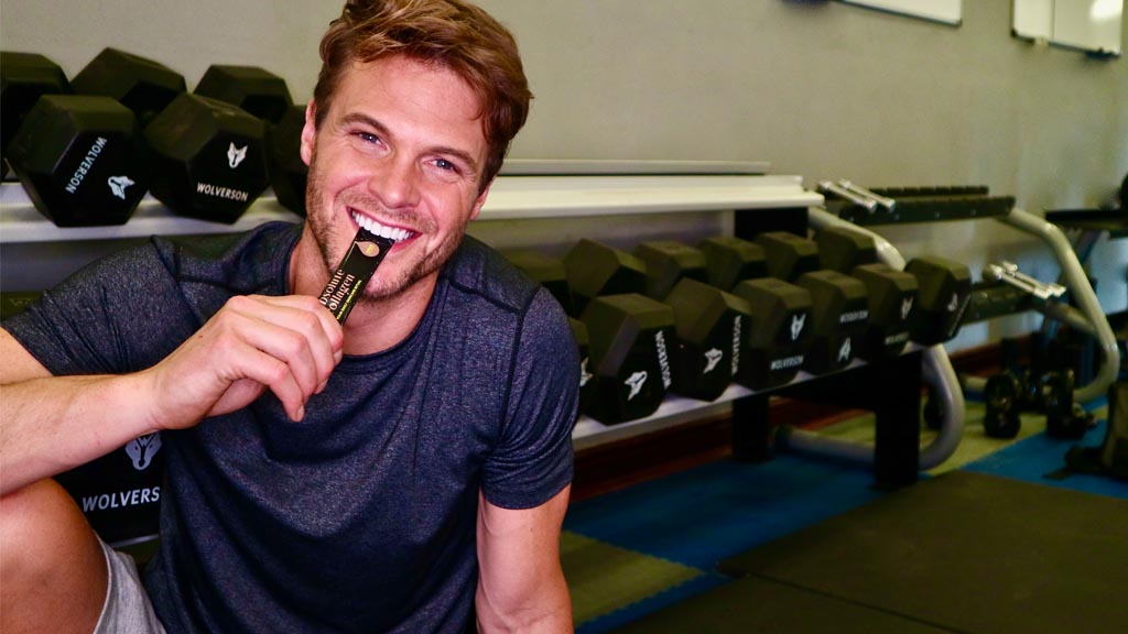 Photo showing a smiling white man in activewear, he is sitting in a gym and taking an Absolute Collagen sachet