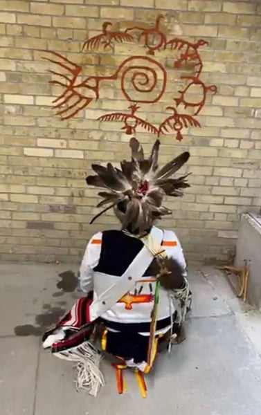 Thomas Sinclair kneeling in full regalia in front of a painting he created on the Royal Ontario Museum walls