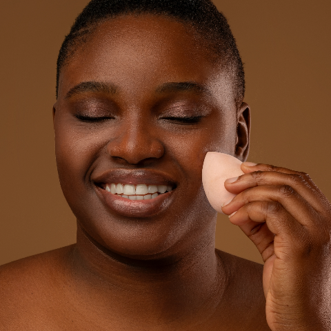 Deeper skin toned model applying foundation with makeup sponge