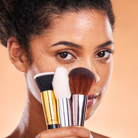 Black model holding makeup brushes in front of face