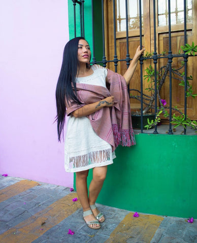 Woman gripping grated window with rebozo wrapped across her back falling over her elbows 