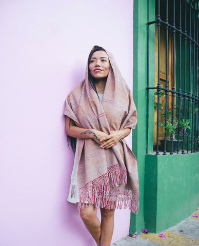 Woman leaning against lilac wall with rebozo wrapped around her head