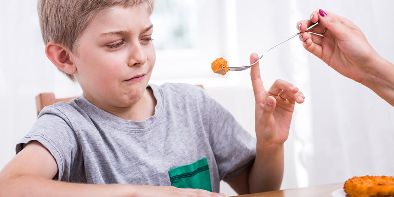 child pushing away food at dinner table