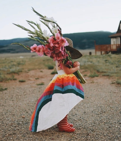 A child wearing the classic rainbow high low while holding a big bouquet of flowers over her face