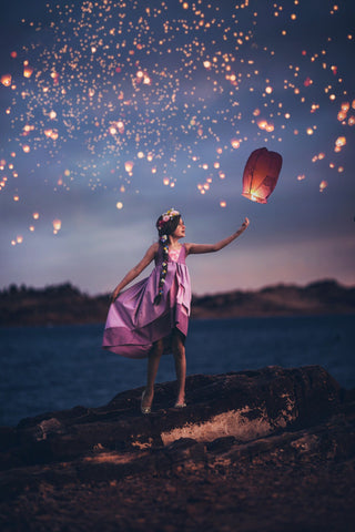 a child wearing the rapunzel dress with a bunch of floating lights behind her