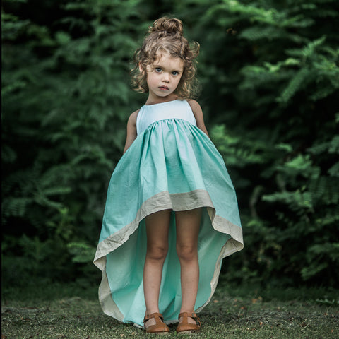 a moody child wearing the mint windsong in front of an emerald green tree line