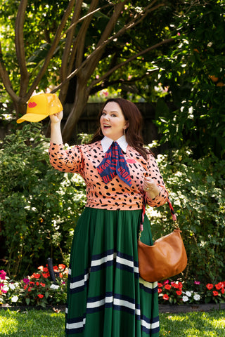 Melissa McCarthy holding the Trucker Hat and Wearing The Cravat, Salmon Jaguar Sweatshirt, and Moyen Messenger From Her Collaboration with Us