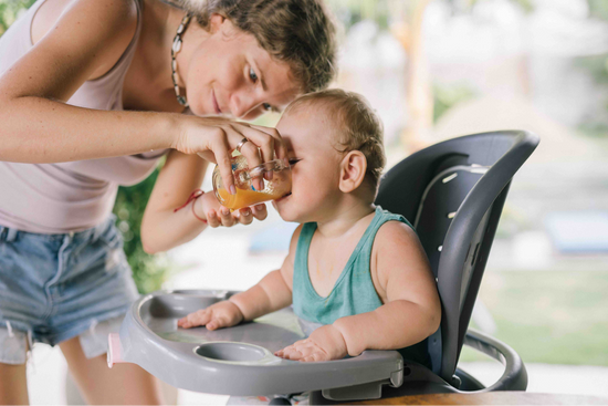 A woman is feeding her baby some juice.