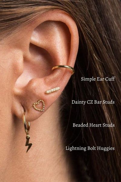 A woman wearing gold heart and lightning bolt earrings.
