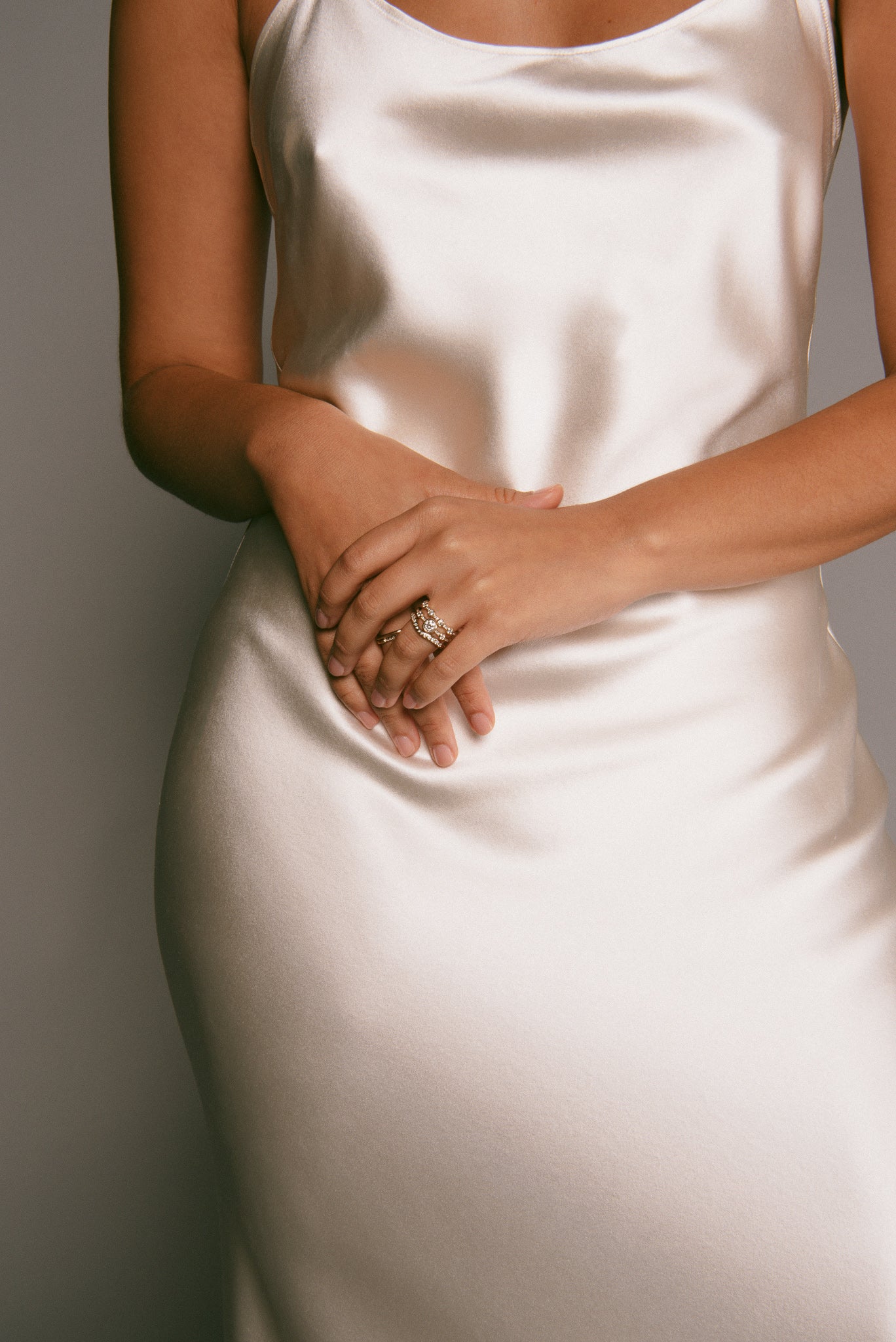 Model in a silk dress, clasping her hands, wearing three bridal-inspired rings.