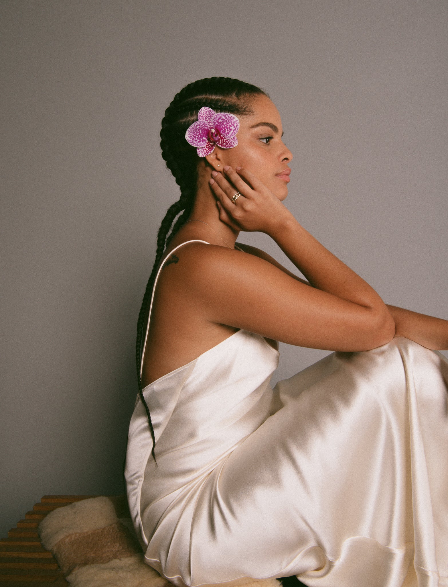 A woman with braids in a silk dress sitting on a shearling-covered bench