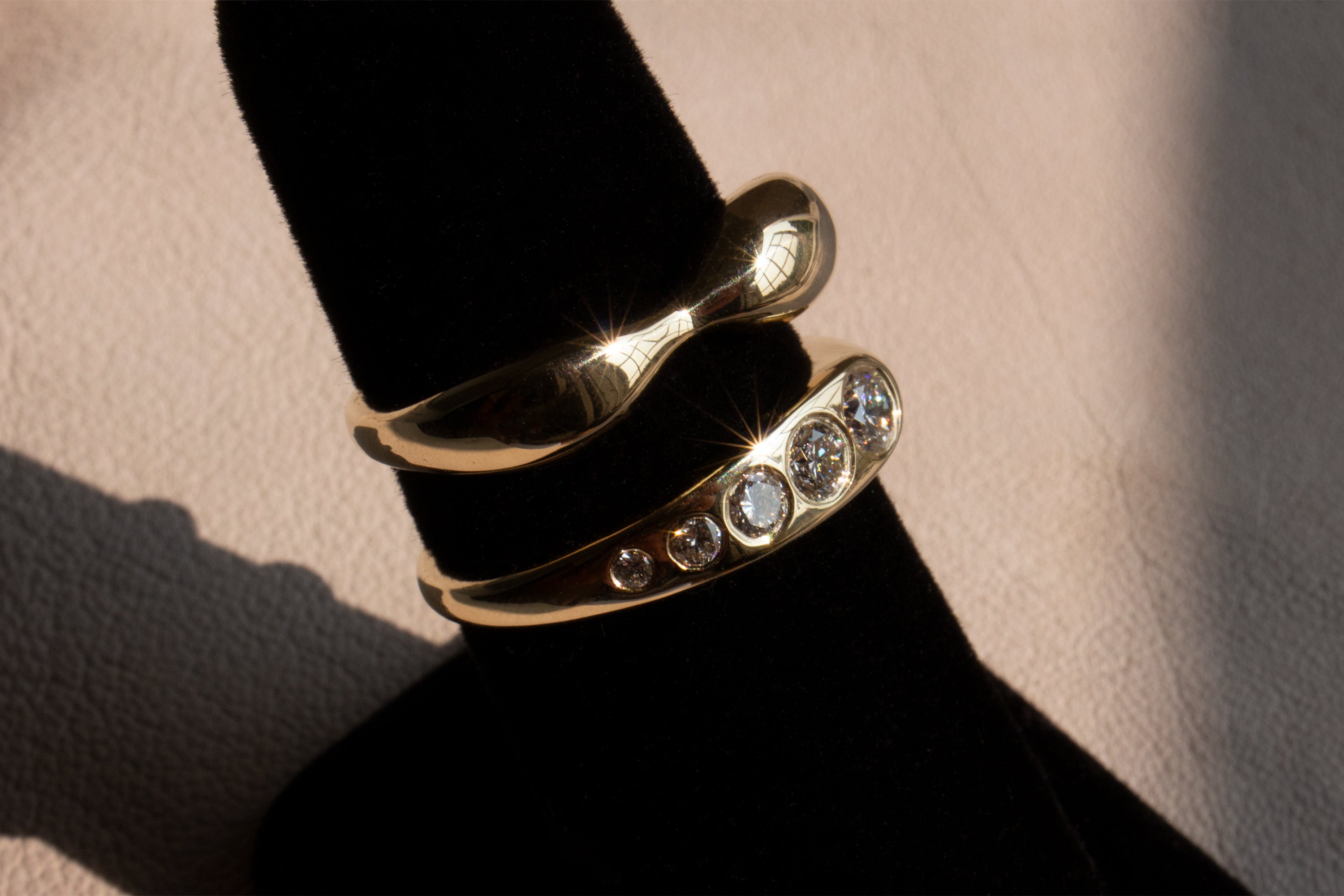 Gold Figure Ring and Grey Diamond Lila Surpima Ring on a ring stand