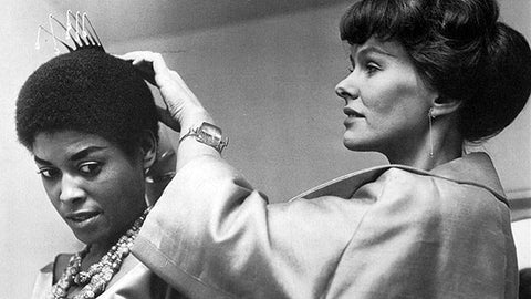 Black and white image of Vivianna Torun Bülow-Hübe fixing a silver comb to the head of singer, songwriter, actor, and activist Abbey Lincoln