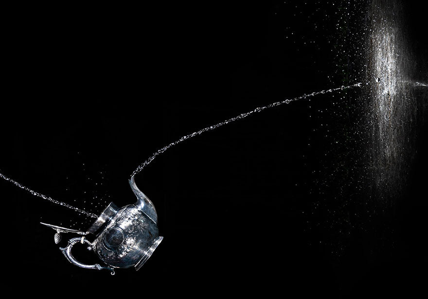 A silver tea kettle pouring water onto a black wall