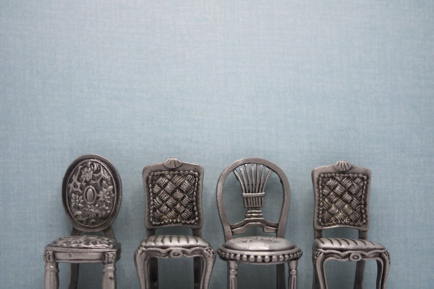 A row of silver antique dollhouse chairs against a dusky blue background