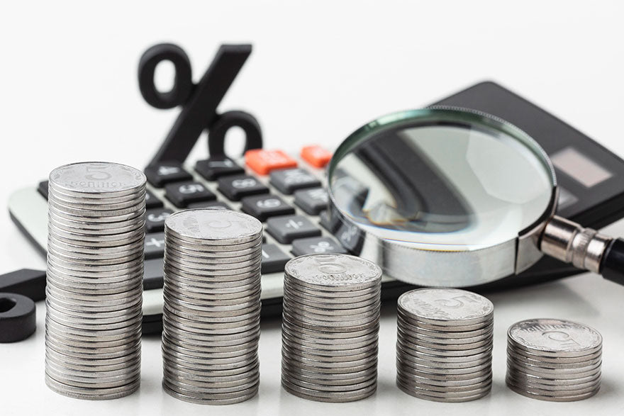 Five stacks of silver coins in front of a calculator and magnifying glass