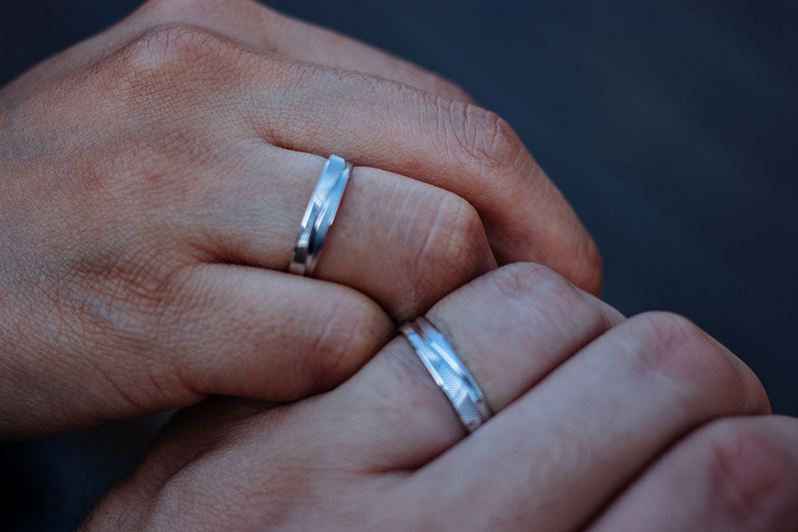 A close-up of two right hands. There’s a silver ring on a finger on each hand.