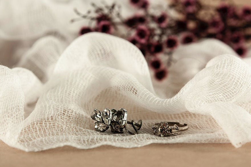 A vintage silver earring and a vintage silver ring sitting on a white ribbon.