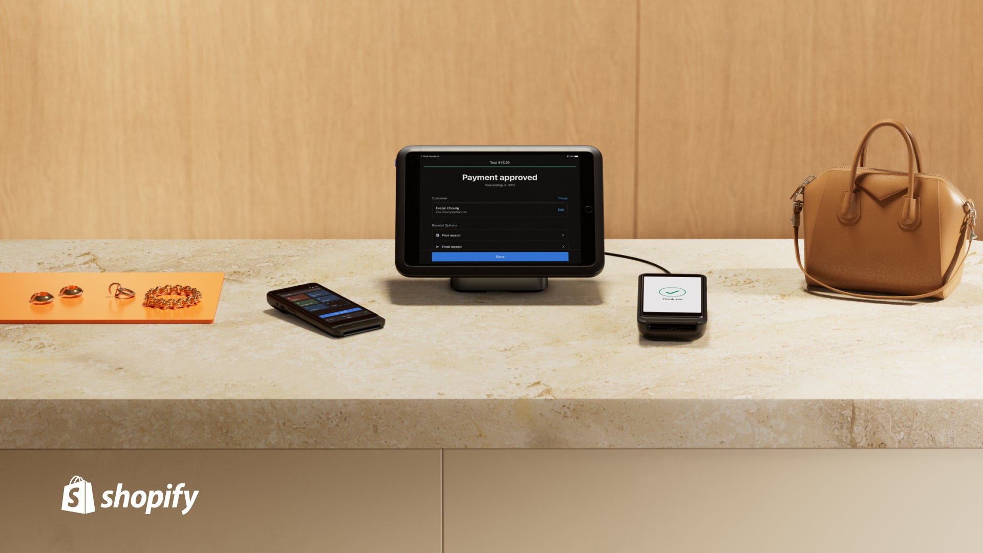 Image of Shopify POS Terminal Countertop Kit on a Store Countertop next to a brown purse on the right side and on the left side a display of jewelry.