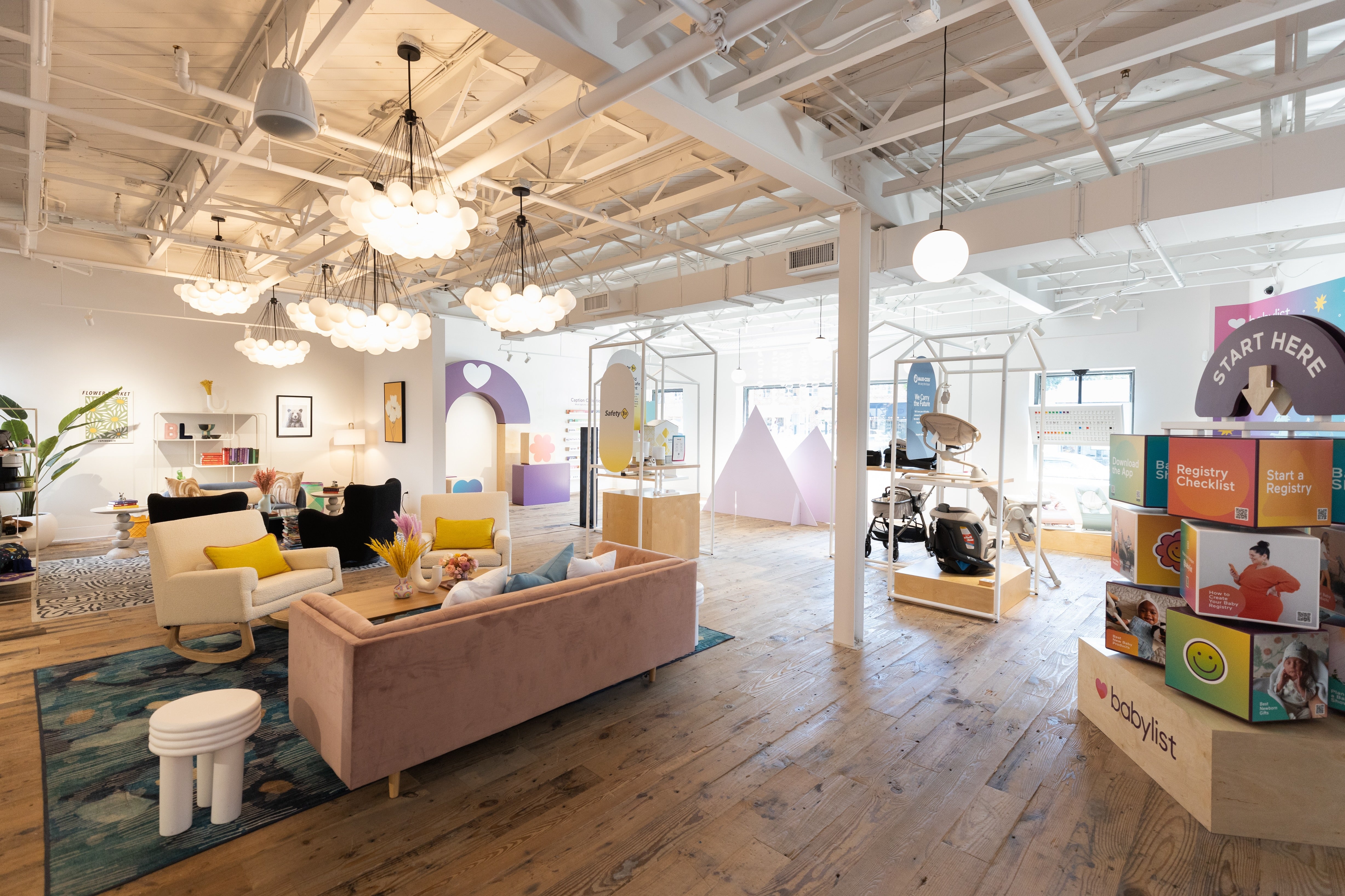 Baby store with colorful baby clothes, toys, and products on display surrounded by bright lights and comfortable, pink couches