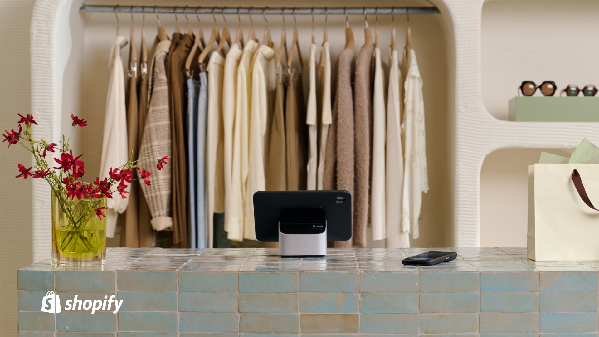 Shopify POS on a checkout stand with clothing hanging on a rack in the background.