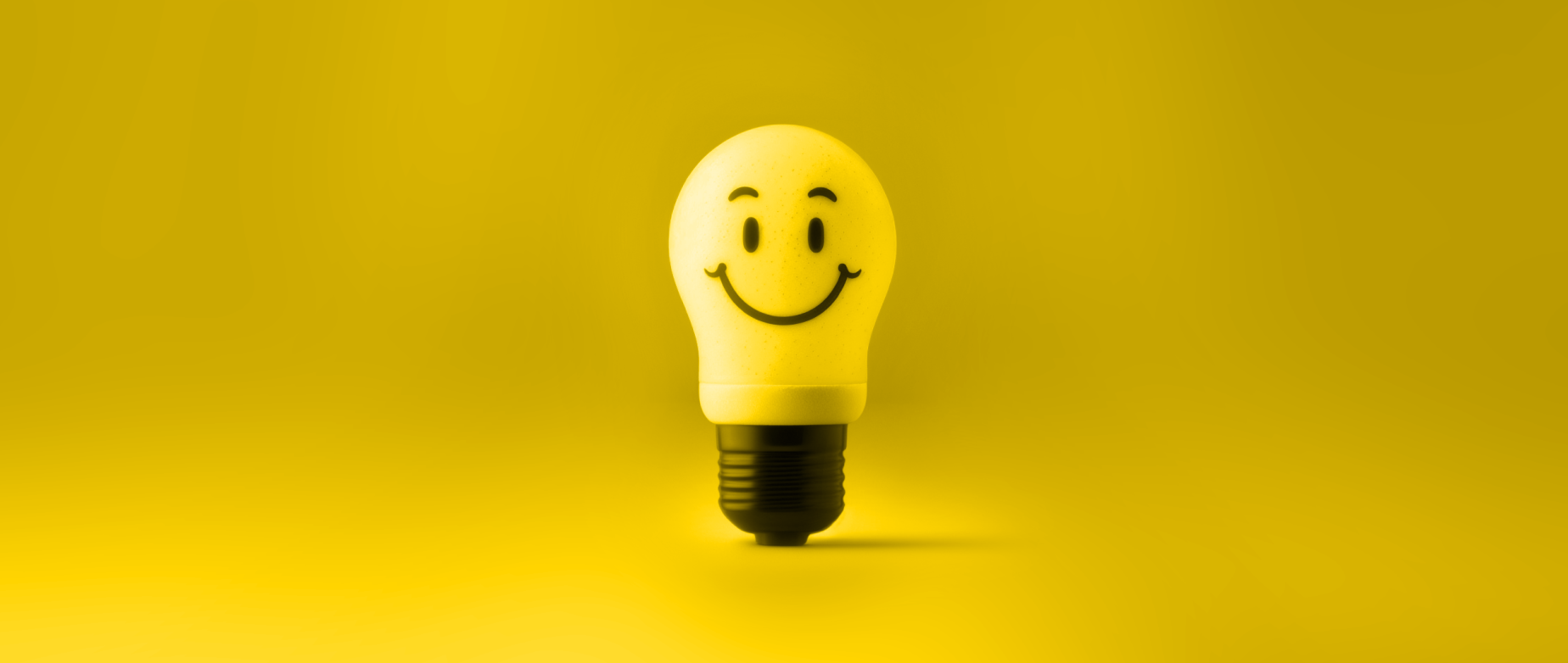 A yellow light bulb with a smiley face on a yellow background.