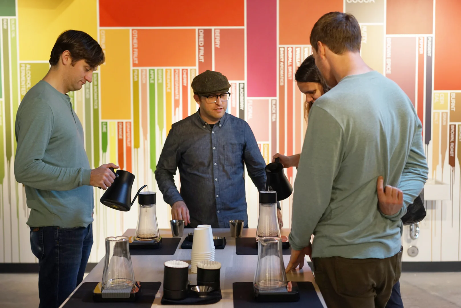 Group of four people brewing coffee in-store against a multi-colored wall