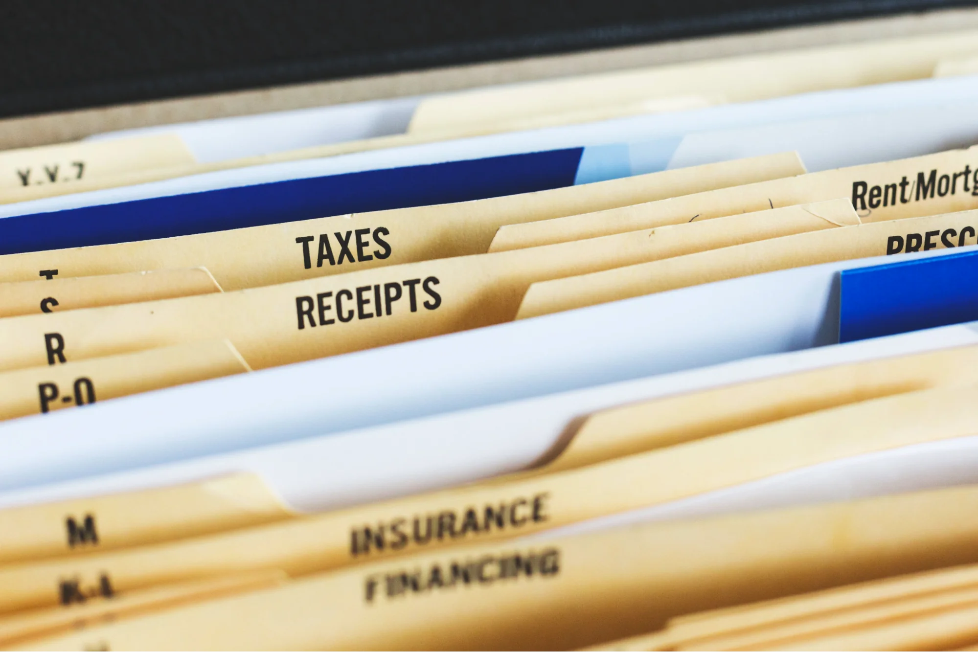 A collection of files in a filing cabinet. Focus is on two files labelled "Taxes" and "Receipts". 