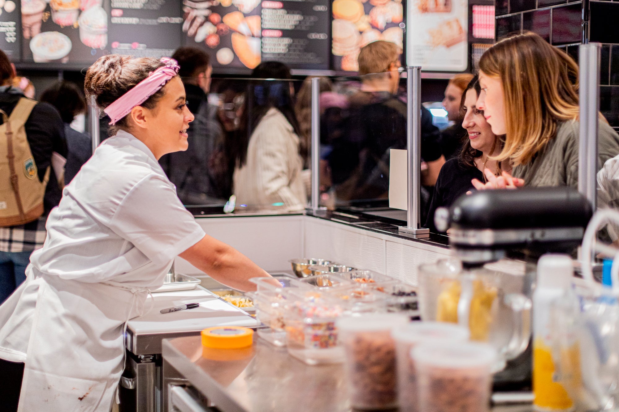 A female baker in a white chef’s jacket prepares customizable dessert at the Milk Bar flagship store