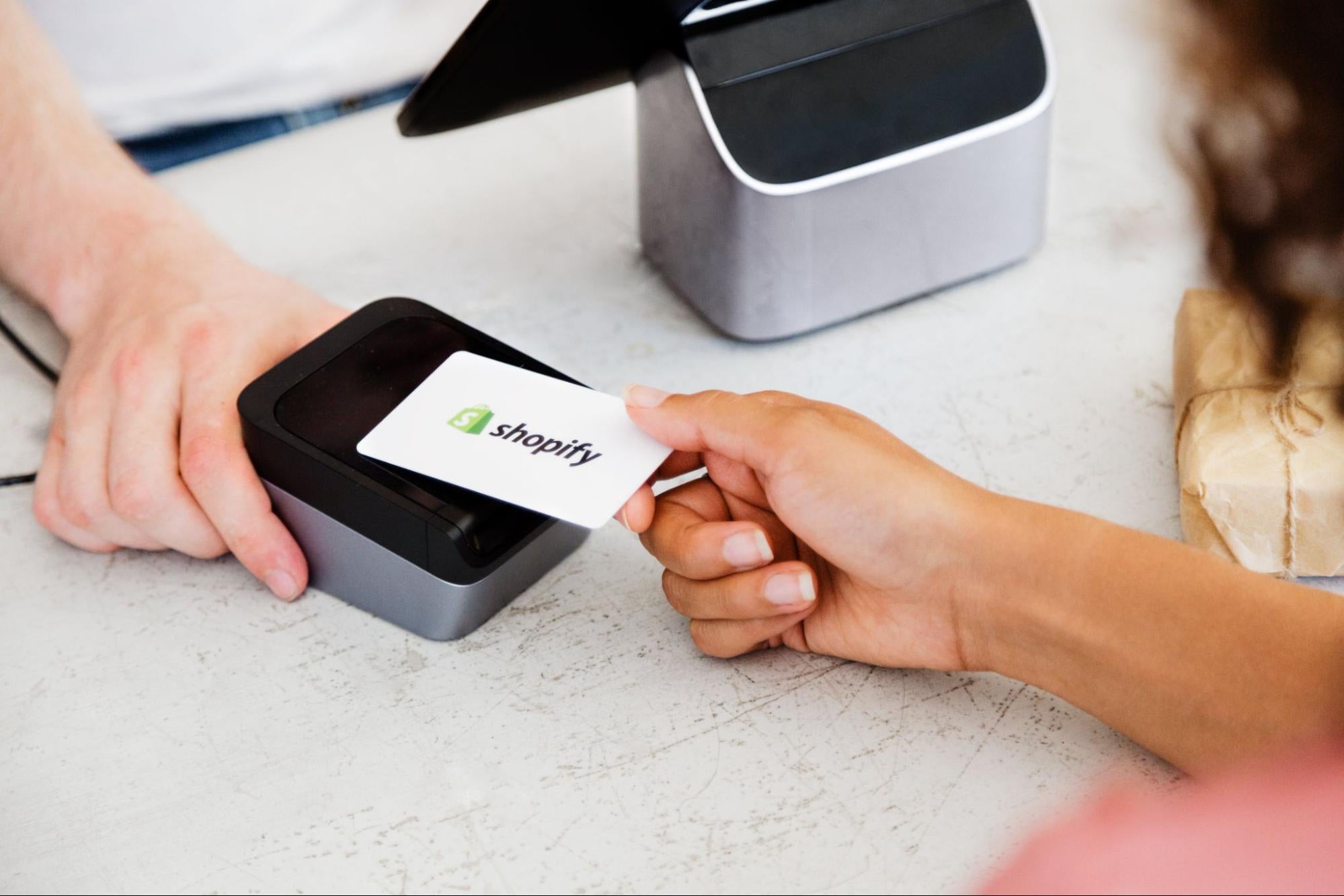 Photo of a woman tapping a Shopify card onto a credit card reader.
