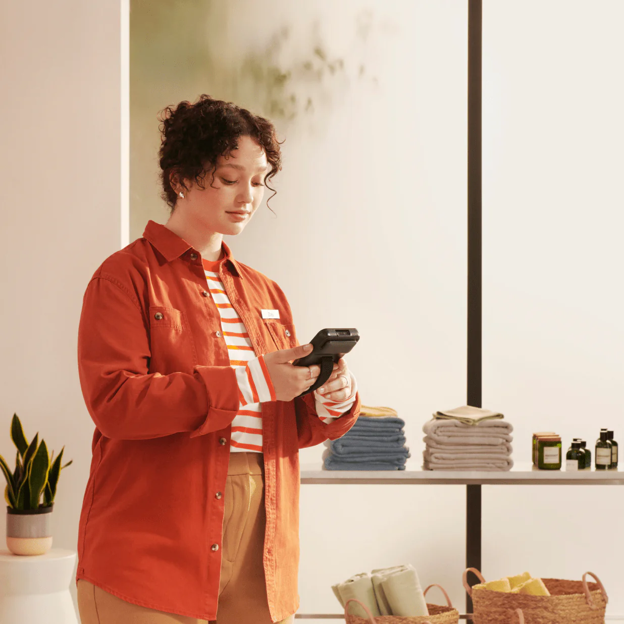 Woman wearing orange jacket looking at Shopify POS in a homewear shop