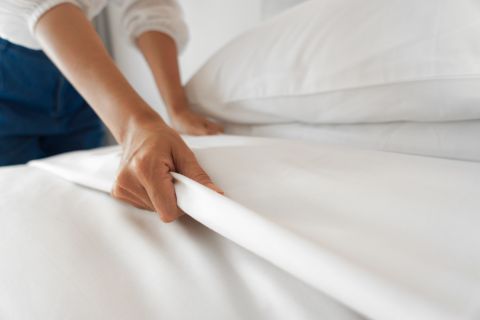 Person putting white sheets on a hotel bed