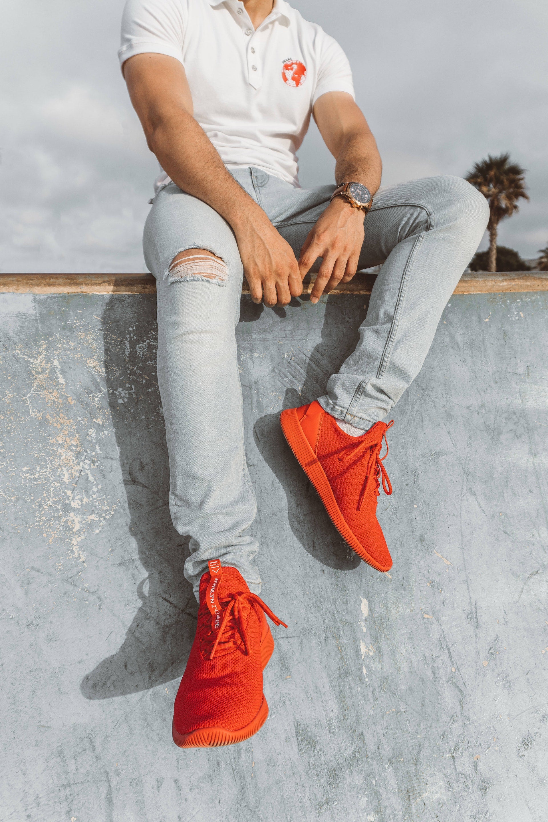 A man sitting on a wall wearing red athleisure shoes