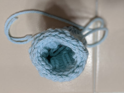 Photo of a knitted tube from the top down in light blue yarn. The top of the tube has an i-cord bind-off that was grafted seamlessly using the kitchener stitch