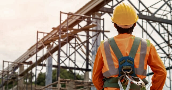 An Australian worker wearing a safety harness inspects industrial scaffolding on a building site.