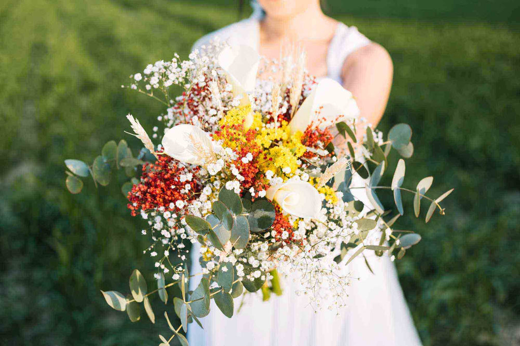 A bride holds a bouquet of red and white small flowers mixed with baby's breaths. 