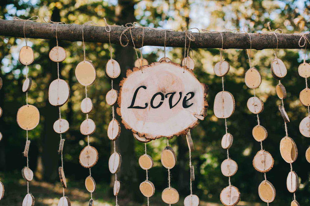 A boho wood sign that reads, "love" hangs from a wood frame with tiny wooden circles in the background. 