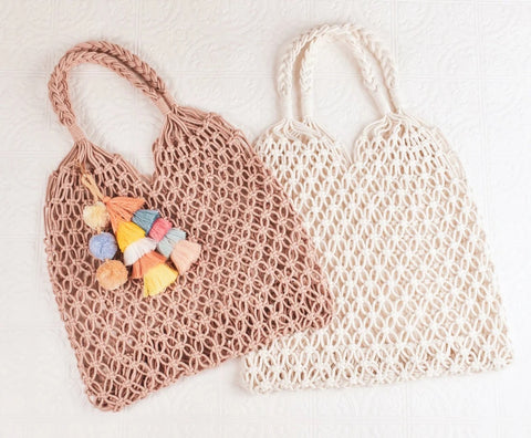 A tan crocheted hand bag with colorful tassels lays on top of a white crocheted hand bag.