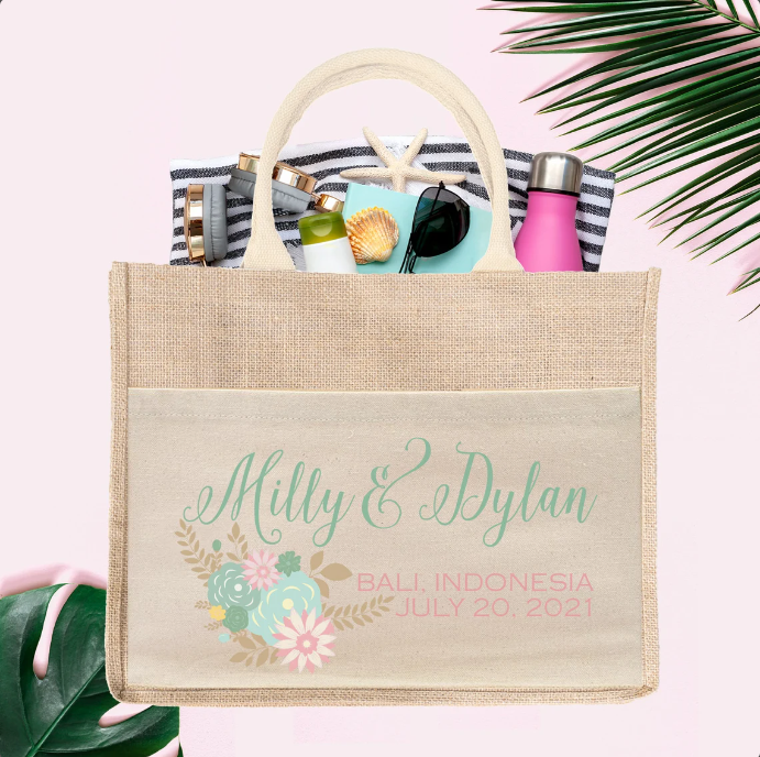 A tan floral destination wedding welcome bag that reads, "Milly& Dylan" spill out sunglasses, sunscreen, sea shells and other cosmetic products.
